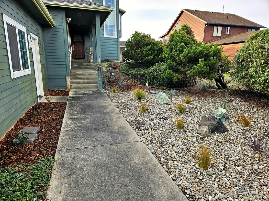 Finished coastal front yard with river-rock beds, ornamental grasses, and a walkway, landscaping by SeaBreeze